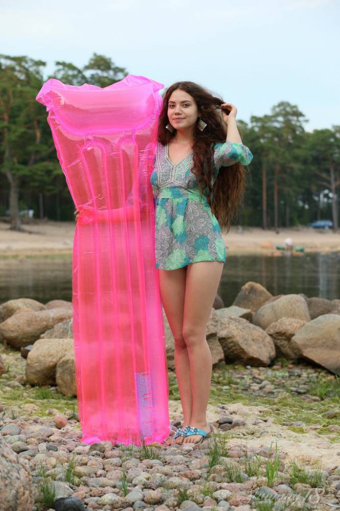 Leggy teen Norma A undresses to pose nude on a pink air mattress by the water - #13