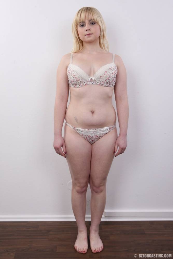Plump blond girl removes her clothes until she's standing naked against a wall - #15