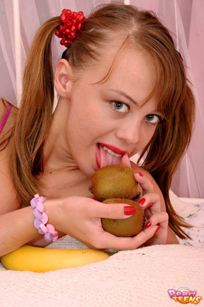 Young looking girl peels and eats a banana on a bed with her hair in pigtails - #1