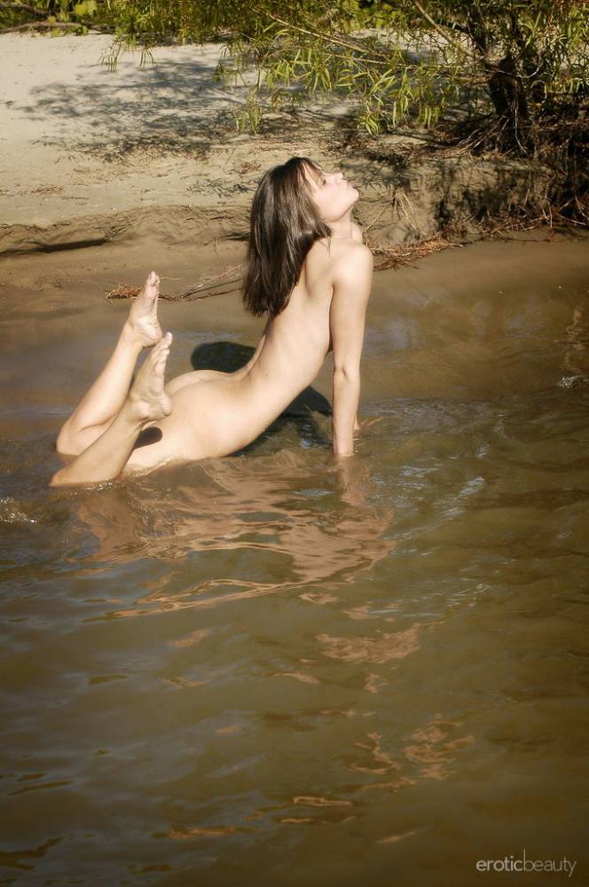 Naked teen with perky tits wades into a shallow river and sits down - #11