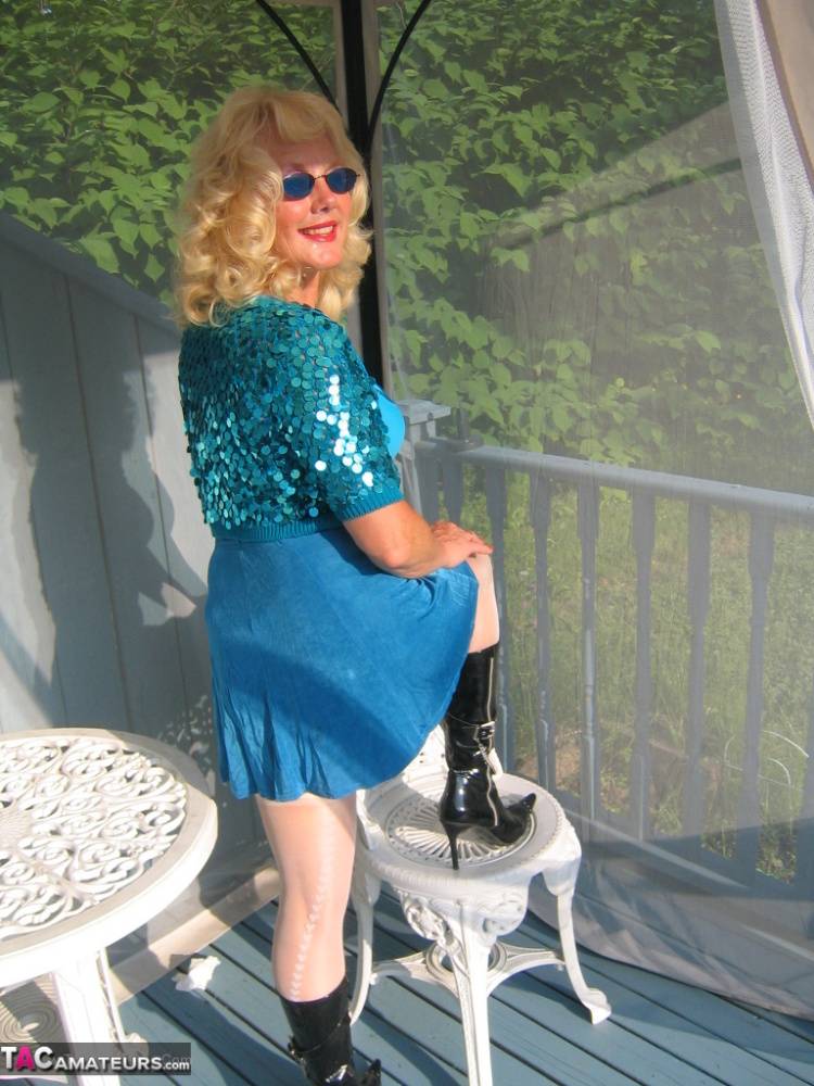 Mature blonde Ruth models a bra and skirt in boots and shades on a deck - #12