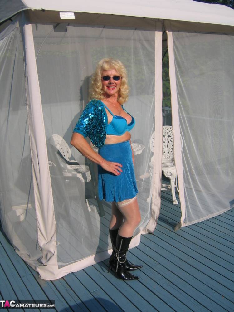 Mature blonde Ruth models a bra and skirt in boots and shades on a deck - #2