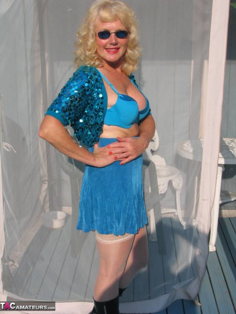 Mature blonde Ruth models a bra and skirt in boots and shades on a deck - #9