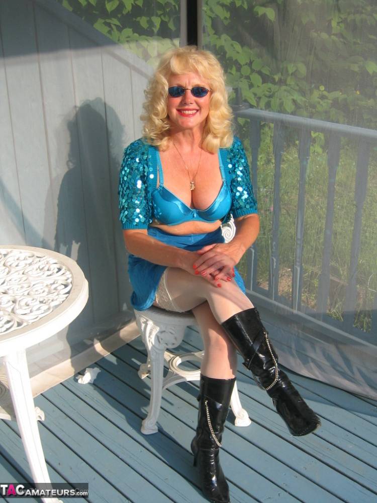 Mature blonde Ruth models a bra and skirt in boots and shades on a deck - #6