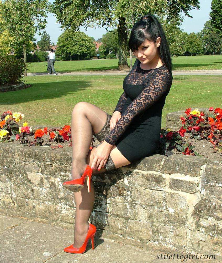 Brunette female in a short dress and stockings dangles red heels on stone wall - #4