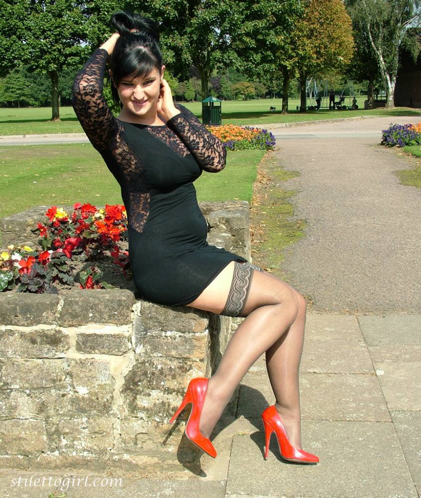 Brunette female in a short dress and stockings dangles red heels on stone wall - #6