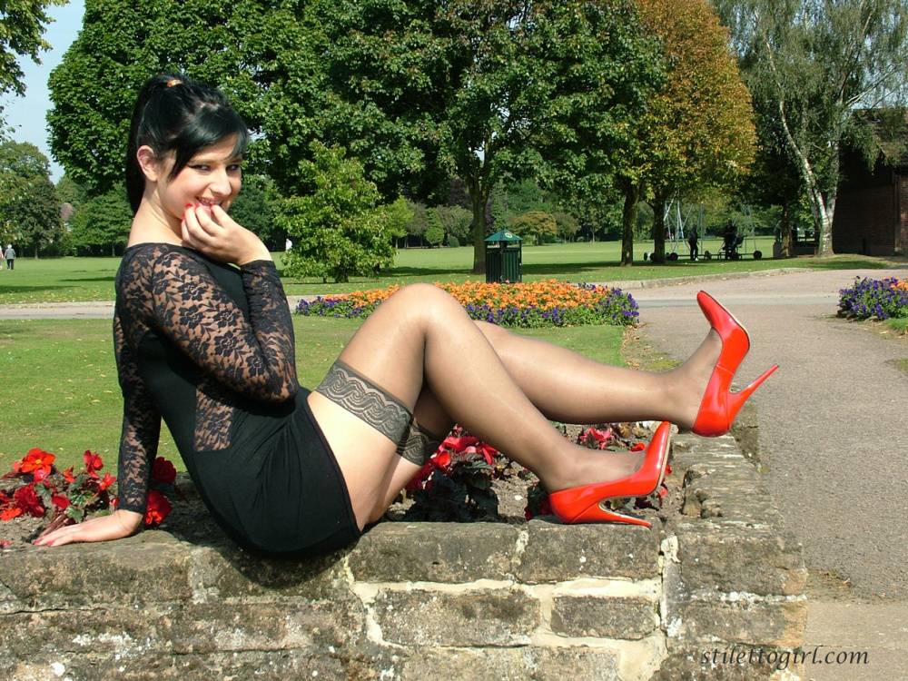 Brunette female in a short dress and stockings dangles red heels on stone wall - #14