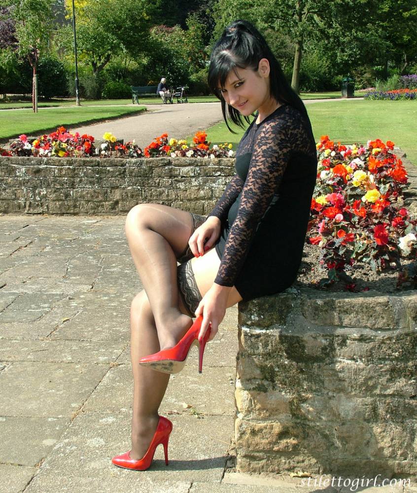 Brunette female in a short dress and stockings dangles red heels on stone wall - #9