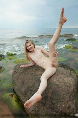 Slim teen Nimfa removes a black bikini to pose naked on seaside rocks on clubgf.com